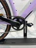 Detail der Kurbelgarnitur und Kette eines violetten Fahrrads, das auf einem Ständer steht.