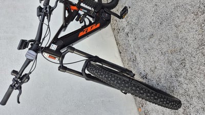Ein schwarzes KTM E-Bike mit orangefarbenem Logo steht auf grauem Untergrund. Ein schwarzes KTM E-Bike mit orangefarbenem Logo steht auf grauem Untergrund.