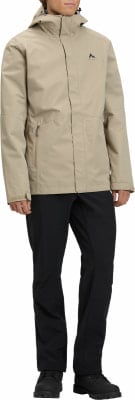 Ein Mann in einer beige Jacke und schwarzen Hosen posiert vor weißem Hintergrund. Ein Mann in einer beige Jacke und schwarzen Hosen posiert vor weißem Hintergrund.