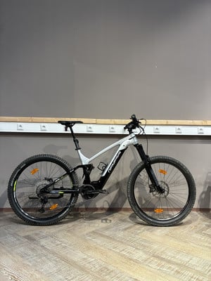 Ein silbernes Genesis E-Mountainbike steht auf einem Holzboden. Ein silbernes Genesis E-Mountainbike steht auf einem Holzboden.