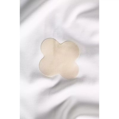 Beige Kleidungspflaster in Kleeblattform auf weißem Stoff. Beige Kleidungspflaster in Kleeblattform auf weißem Stoff.