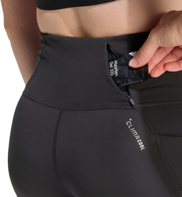 Eine Frau verstaut ein Energiegel in einer Reißverschlusstasche an ihrer Leggings. Eine Frau verstaut ein Energiegel in einer Reißverschlusstasche an ihrer Leggings.