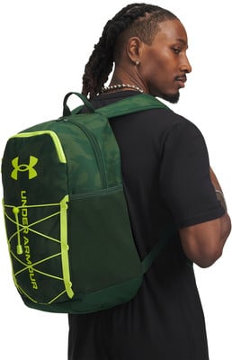 Ein Mann mit Zöpfen trägt auf dem Rücken einen grünen Rucksack mit Under Armour Logo. Ein Mann mit Zöpfen trägt auf dem Rücken einen grünen Rucksack mit Under Armour Logo.