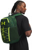 Ein Mann mit Zöpfen trägt auf dem Rücken einen grünen Rucksack mit Under Armour Logo.