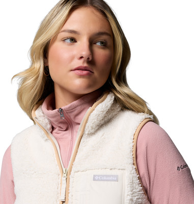 Eine Frau in einer cremefarbenen Fleeceweste und einem rosafarbenen Kapuzenpullover.