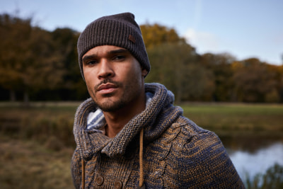Ein Mann in einer Mütze und einem Strickpullover blickt in die Kamera. Ein Mann in einer Mütze und einem Strickpullover blickt in die Kamera.