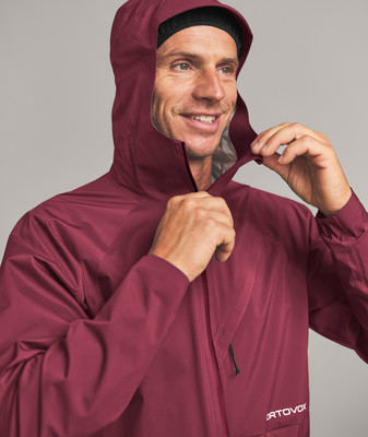 Ein Mann in einer dunkelroten Kapuzenjacke passt den Kragen an.