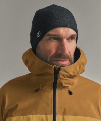 Ein Mann mit dunkler Mütze und brauner Kapuzenjacke blickt zur Seite. Ein Mann mit dunkler Mütze und brauner Kapuzenjacke blickt zur Seite.