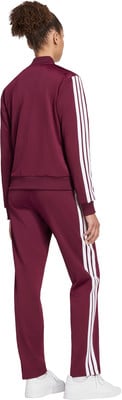 Eine Frau in einem dunkelroten Adidas-Anzug mit weißen Streifen und weißen Turnschuhen.