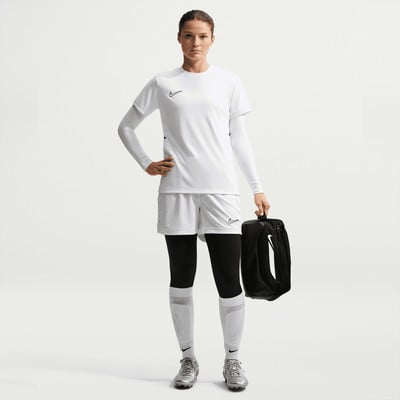 Eine Frau in weißer Fußballkleidung mit einem Rucksack in der Hand.