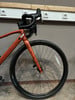 Vorderseite eines orangefarbenen Fahrrads mit Lenker und Vorderrad.