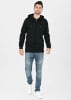 Ein Mann in einem schwarzen Kapuzenpullover mit Reißverschluss, blauer Jeans und weißen Sneakern.