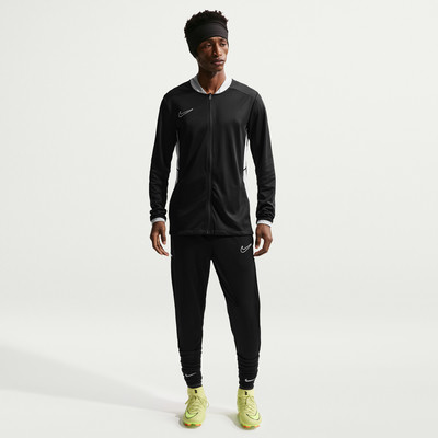 Ein Mann in schwarzer Nike Sportbekleidung mit weißen Akzenten und gelben Fußballschuhen. Ein Mann in schwarzer Nike Sportbekleidung mit weißen Akzenten und gelben Fußballschuhen.