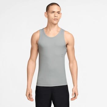 Ein Mann im grauen Tanktop und schwarzer Hose posiert vor hellem Hintergrund.