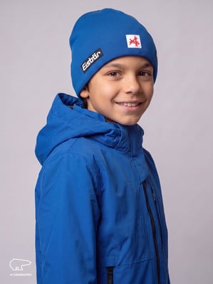 Ein Junge in einer blauen Winterjacke und Mütze mit Eisbär-Logo lächelt. Ein Junge in einer blauen Winterjacke und Mütze mit Eisbär-Logo lächelt.