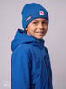 Ein Junge in einer blauen Winterjacke und Mütze mit Eisbär-Logo lächelt.