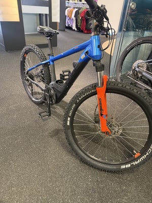 Ein blaues E-Mountainbike mit oranger Gabel auf dunklem Untergrund. Ein blaues E-Mountainbike mit oranger Gabel auf dunklem Untergrund.