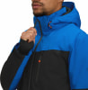 Ein Mann schließt eine blaue Jacke mit schwarzen Ärmeln und orangefarbenen Details.