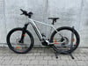 Ein silbernes E-Mountainbike mit schwarzen Rädern vor einer Betonwand.