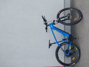 Ein blaues Mountain-E-Bike der Marke Genesis, das an einer grauen Wand geparkt ist.