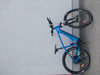 Ein blaues Mountain-E-Bike der Marke Genesis, das an einer grauen Wand geparkt ist.