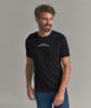 Ein Mann in einem schwarzen T-Shirt mit Bergmotiv und blauer Hose.