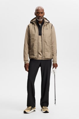 Ein Mann in einer beige Weste und schwarzen Hose hält einen Golfschläger.