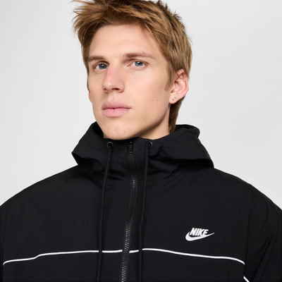 Muž v černé bundě Nike s bílým logem a pruhy na hrudi. Muž v černé bundě Nike s bílým logem a pruhy na hrudi.