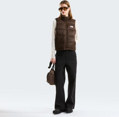 Model in brauner Weste und schwarzer Hose mit Umhängetasche.