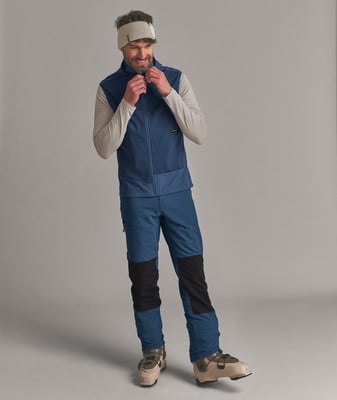 Ein Mann in einer blauen Weste und Hose mit Skischuhen vor grauem Hintergrund. Ein Mann in einer blauen Weste und Hose mit Skischuhen vor grauem Hintergrund.