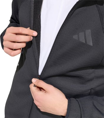 Ein Mann öffnet eine schwarze Jacke mit Adidas-Logo auf der Brust.