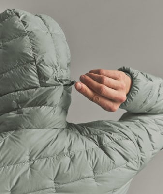 Eine Hand verstellt den Kapuzenzug einer Daunenjacke. Eine Hand verstellt den Kapuzenzug einer Daunenjacke.