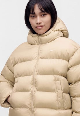 Žena v béžové péřové bundě s kapucí a logem Nike.