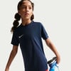Ein Mädchen im dunkelblauen Nike-T-Shirt dehnt ihr Bein, während sie wegschaut.