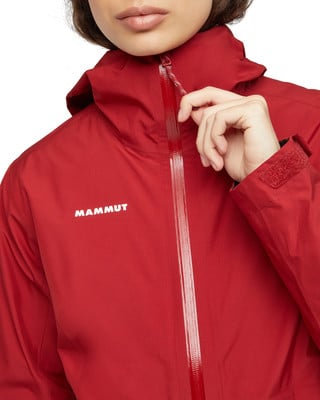 Eine Frau schließt eine rote Jacke mit Mammut-Logo und Kapuze. Eine Frau schließt eine rote Jacke mit Mammut-Logo und Kapuze.