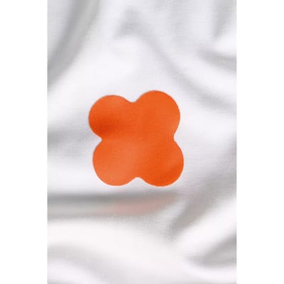 Ein orangefarbenes Kleeblatt auf weißem Stoffhintergrund. Ein orangefarbenes Kleeblatt auf weißem Stoffhintergrund.