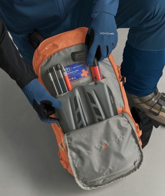 Eine Person räumt eine Lawinenschaufel und Sonde in einen orangefarbenen Rucksack. Eine Person räumt eine Lawinenschaufel und Sonde in einen orangefarbenen Rucksack.