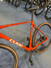 Ein orangefarbenes Cube Gravelbike mit braunen Reifen steht auf einem blauen Teppich.