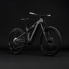 Graues E-Bike mit Federung und schwarzen Rädern auf dunklem Hintergrund.