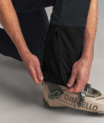 Ein Mann schließt seine Skihose an den Schnallen seiner Skischuhe.