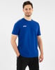 Ein Mann in einem blauen T-Shirt und schwarzen Trainingshosen steht mit der Hand in der Tasche.