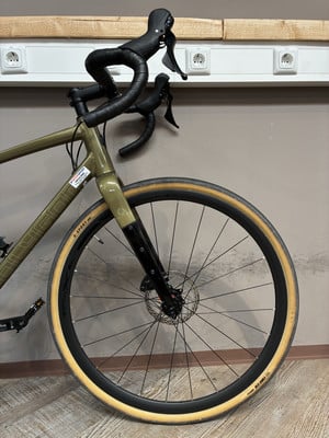 Ein grünes Gravelbike mit schwarzem Lenker und beigen Reifen steht an der Wand. Ein grünes Gravelbike mit schwarzem Lenker und beigen Reifen steht an der Wand.