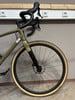 Ein grünes Gravelbike mit schwarzem Lenker und beigen Reifen steht an der Wand.