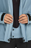 Detail von Händen, die eine blaue Jacke mit schwarzem Kragen und Klettverschluss schließen.