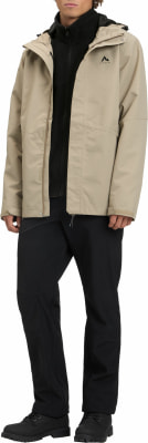 Ein Mann in einer beigen Jacke und schwarzen Hosen steht in Stiefeln. Ein Mann in einer beigen Jacke und schwarzen Hosen steht in Stiefeln.