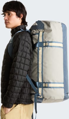 Ein Mann mit schwarzer Steppjacke und beiger Hose trägt einen großen grauen und blauen Rucksack. Ein Mann mit schwarzer Steppjacke und beiger Hose trägt einen großen grauen und blauen Rucksack.