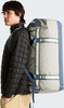 Ein Mann mit schwarzer Steppjacke und beiger Hose trägt einen großen grauen und blauen Rucksack.