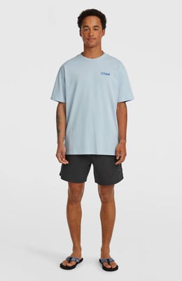 Ein Mann in einem blauen T-Shirt und schwarzen Shorts steht vor einem weißen Hintergrund.