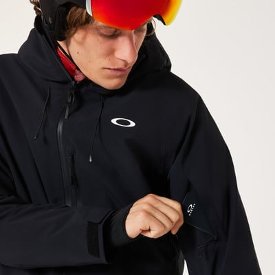 Ein Mann in einer schwarzen Oakley-Skijacke steckt eine Karte in die Tasche.