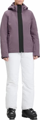 Eine Frau in einer lila Skijacke und weißer Hose mit Skischuhen.